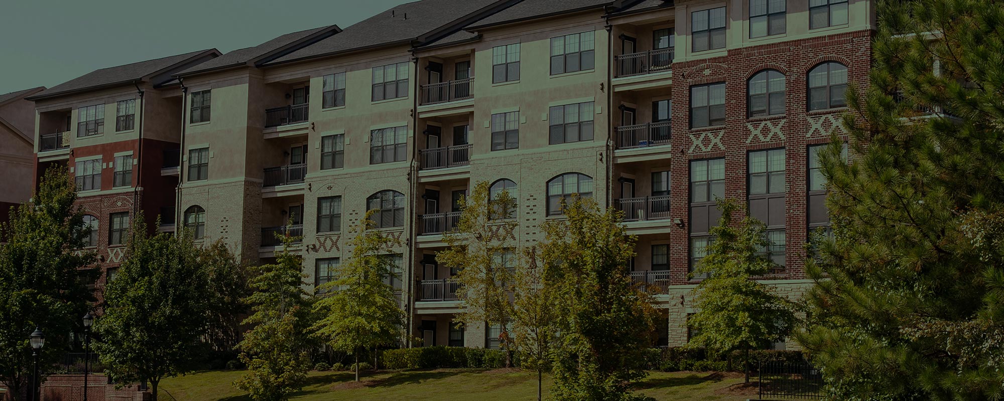 a mid-rise apartment complex behind a lawn and trees